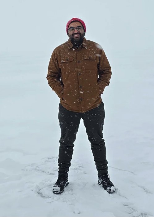 Arslan smiling in a red beanie and brown jacket in falling snow